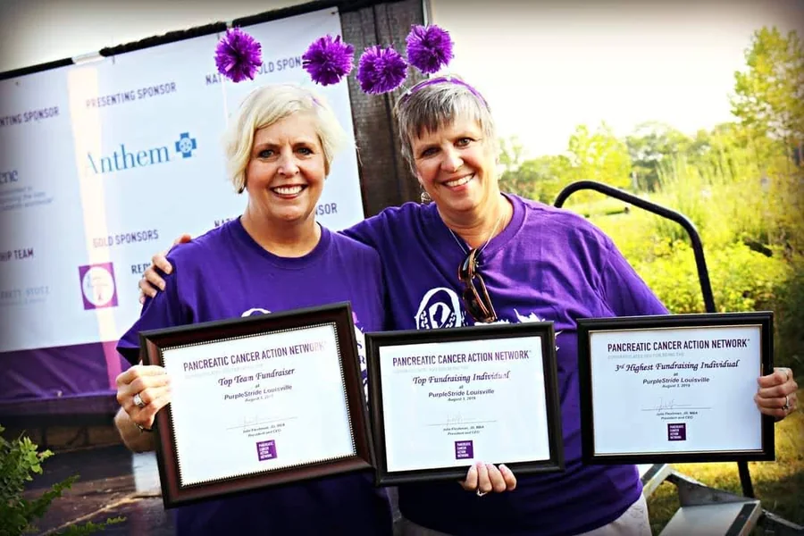 Two supporters in purple holding three PanCAN PurpleStride fundraising awards