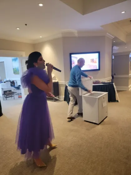 A guest in a purple dress speaking into a microphone at the Sip & Swirl auction