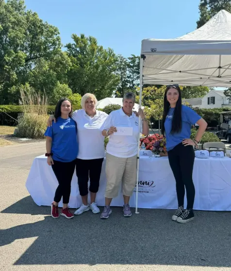 Four people standing at a table under a tent at the golf outing