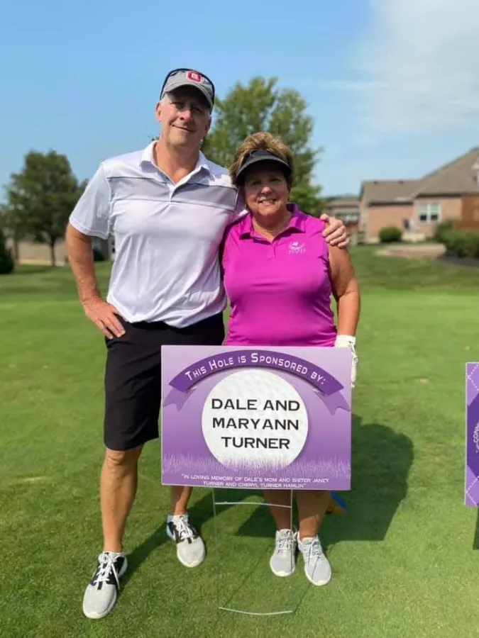 Two golfers standing behind a purple hole sponsor sign on the course