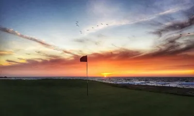 Sunset over the ocean behind a putting green with a flag